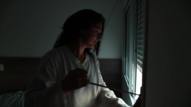Woman closing window blind, making room pitch black
