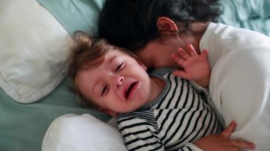 Upset baby infant having a tantum in morning bed. Angry toddler tearful child boy cries having tantrum