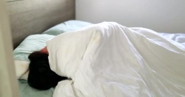 Woman waking up in the morning. Person lying in bed under the sheets wakes up