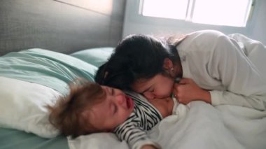 Mother trying to make crying infant baby laugh in morning, casual authentic parent and child relationship