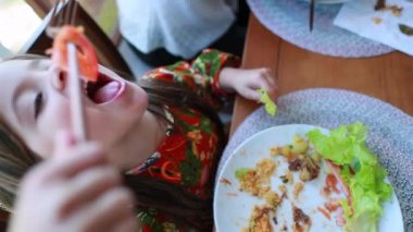 Little girl eating lunch. Child eating salad, healthy meal. Funny kid eating tomato