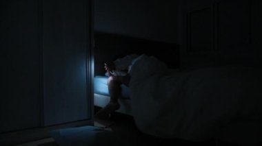 Woman shining light in the dark in bed, girl waking up in the middle of the night looking for something in closet with flashlight