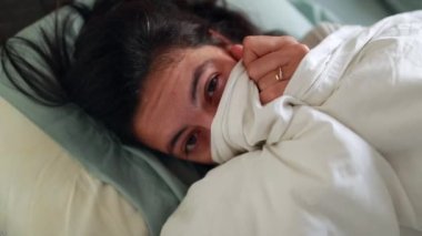 Funny woman playing peekaboo with bed sheets in morning, fun playful girl revealing face smiling in bed