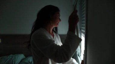 Woman opening window blinds roller, girl waking up in morning looking out window