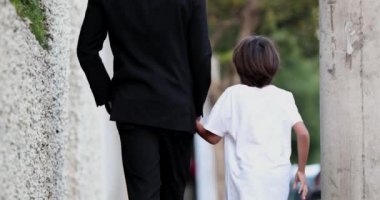 Baba, kaldırımda yürüyen çocukla el ele tutuşuyor.