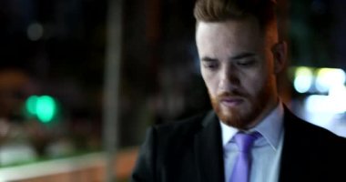 İş adamı yüzü gece yürürken akıllı telefona bakıp gülümsüyor.