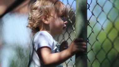 Child watching game leaning on fence, video 