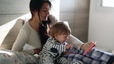 Baby and mother together in bed in the morning holding smartphone device