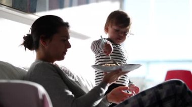 Mother teaching baby to hold fork. Mom and toddler eating breakfast in morning together