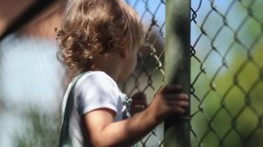 Child watching game leaning on fence, video 