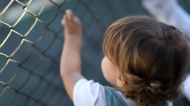 Child watching game leaning on fence, video 