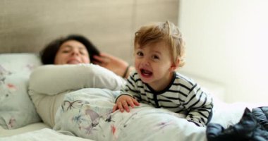 Sweet baby smiling at camera in morning bed with mom