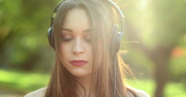Parkta kulaklık takan güzel bir kız müzik, şarkı, podcast ya da sesli kitap dinliyor.