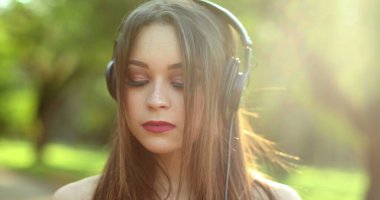 Parkta kulaklık takan güzel bir kız müzik, şarkı, podcast ya da sesli kitap dinliyor.