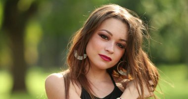 Güzel bir milenyum genç kadın park alanında poz veriyor, kameraya bakıyor.