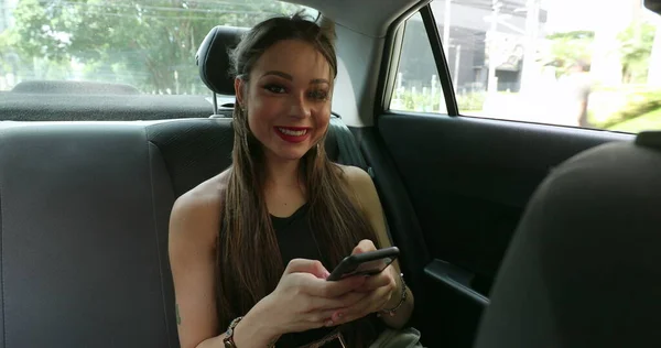 Woman in backseat taxi car smiling to camera, girl holding tech smartphone device