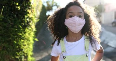 Covid-19 maskeli melez kız kameraya bakıyor.