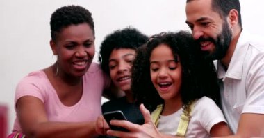 Irklar arası aile ve çocuklar birlikte gülüyor. Ev koltuğunda cep telefonuna bakıyorlar.