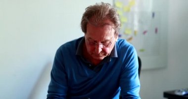 Serious Candid older man working from home using cellphone device, focused concentrated senior worker