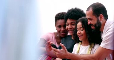 Interracial parents and ethnically diverse kids laughing at social media content on cellphone