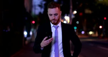 Irish Business man walking at night staring at smartphone, corporate executive at night city sidewalk