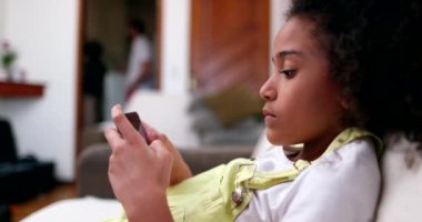 Evdeki koltukta akıllı telefon kullanan küçük siyah kız. Afrika etnik kökeni