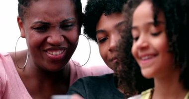 Happy multiracial family laughing and smiling together looking at phone. Real life parents and kids laugh and smile