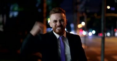 Mutlu iş adamı gece şehirde yürüyor başarıyı kutluyor yumruk kaldırıyor tezahürat yapıyor