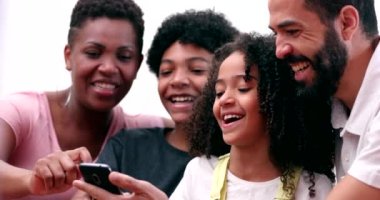 Happy multiracial family laughing and smiling together looking at phone. Real life parents and kids laugh and smile