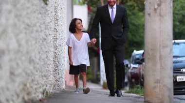 Happy father and son walking together holding hands on sidewalk. Diverse mixed race child and dad
