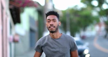 Genç siyahi adam dışarıda kameraya bakıyor. Melez ırk kökenli.