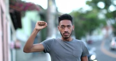 Individual young black man raising fist in air staring camera in protest. Rebel African mixed race ethnicity