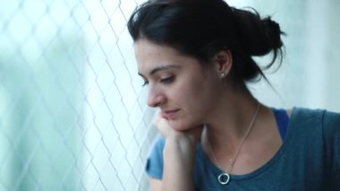 Contemplative woman looking out through balcony window. Pensive person staying at home