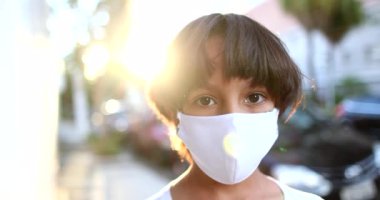 Güneş ışığında dışarıda Coronavirus maskesi takan farklı etnik kökenli bir çocuk, açık havada cerrahi maske takan melez bir çocuk portresi.