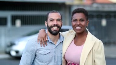 Mixed race couple smiling at camera, married ethnically diverse wife and husband outside in street