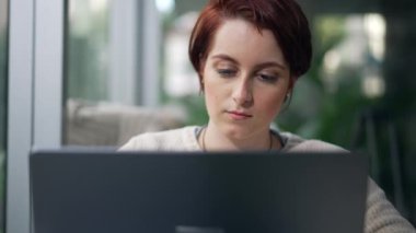 Yakından, kahve dükkanında oturan dizüstü bilgisayarın önünde gülümseyen genç bir kadın yüzü.