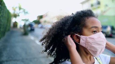 Little girl putting covid-19 face mask walking outside in city sidewalk, mix race child