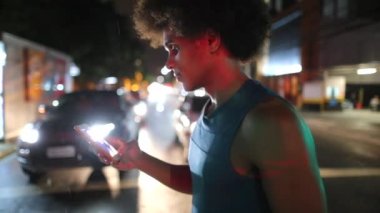 Young black man checking smartphone while crossing city street at night