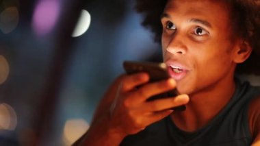 Young black man sending voice message with cellphone device at night in the city