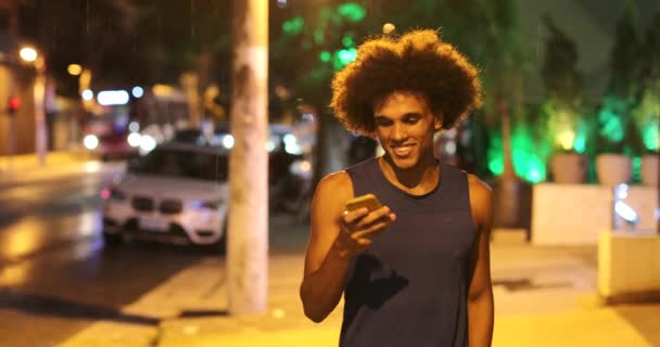 Молодий Африканський Чоловік Ходить Вночі Місті Дивлячись Мобільний Пристрій Посміхаючись — стокове відео