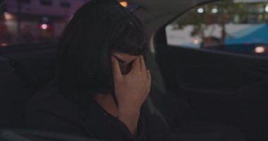 Upset young woman covering face with shame while riding taxi cab in the backseat of car. One anxious hispanic girl feeling overwhelmed by modern pressure. Unhappy Person suffering from anxiety and loneliness