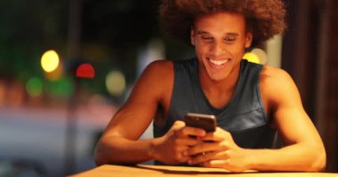 Casual young african american man holding smartphone smiling and laughing candid