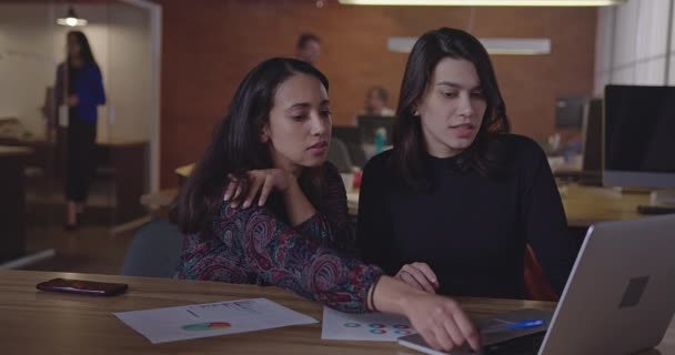 現代の職場で夜にノートパソコンの前で仕事について話している若いビジネスマンの女性 新しい従業員に仕事を説明する女性同僚 女性は夜に残業する新しい戦略を計画 — ストック動画