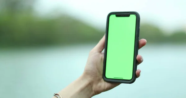 Hand holding smartphone device with greenscreen. Chroma key, close up woman hand holding phone with vertical green screen