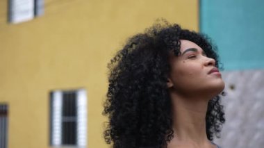 A contemplative black woman standing outside looking at sky in street