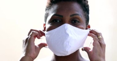 African woman putting covid face mask, black ethnicity female looking at camera