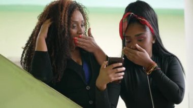 Mother and daughter reacting with shock to content online holding smartphone two people surprise reaction