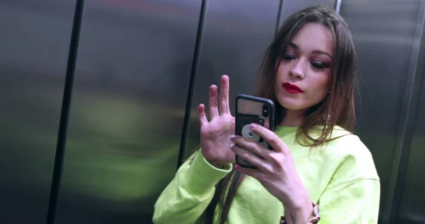 아가씨가 엘리베이터 앞에서 핸드폰으로 사진을 있어요 매력적 여자가 셀카를 받아들인다 — 스톡 사진