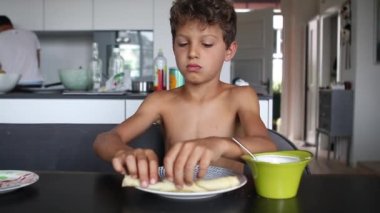 Child eating pancake in morning breakfast table