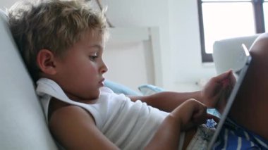 Child sitting in sofa looking at tablet device. Young boy using tech tablet